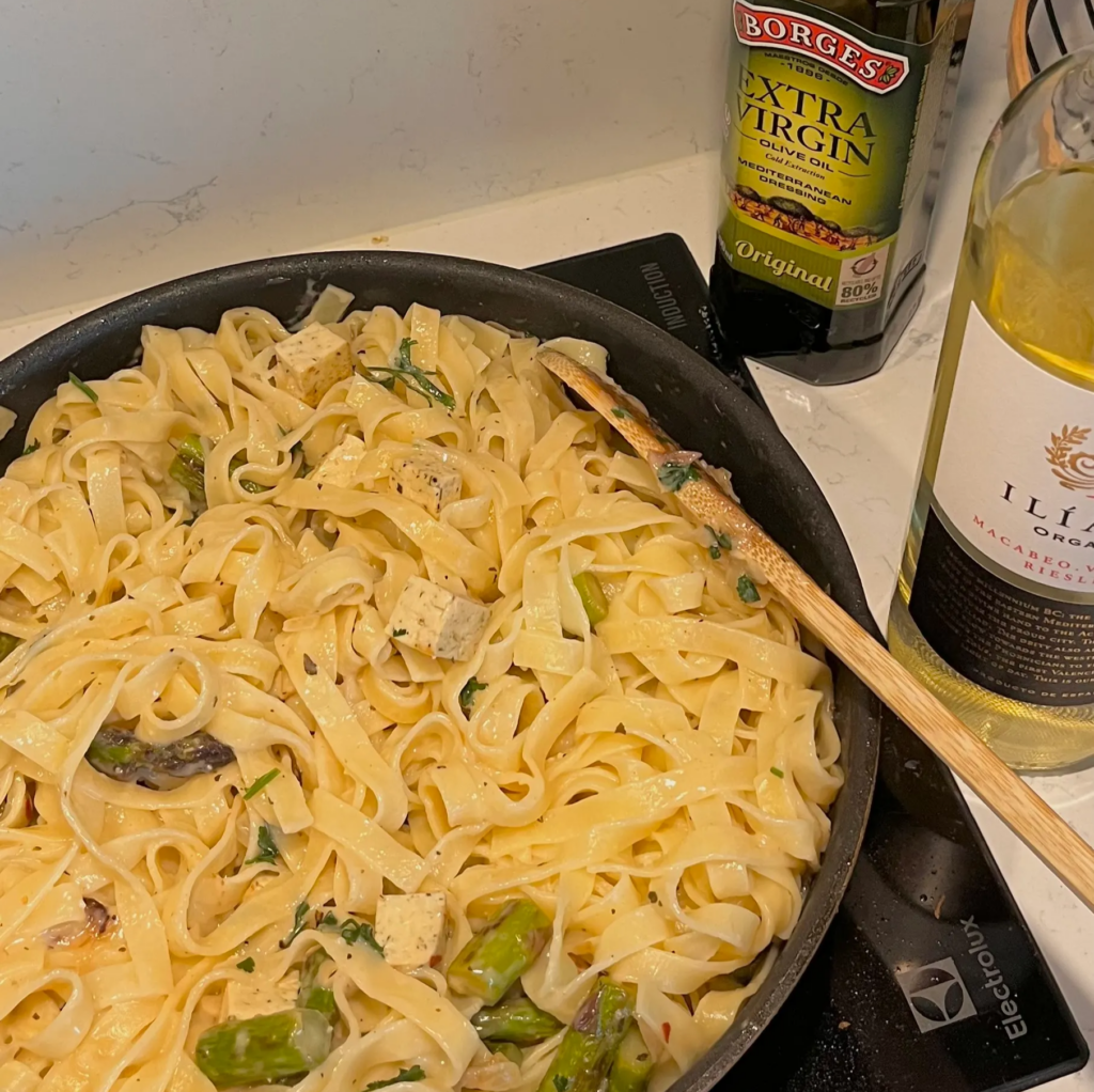 pasta cooking in a pan next to a bottle of olive oil